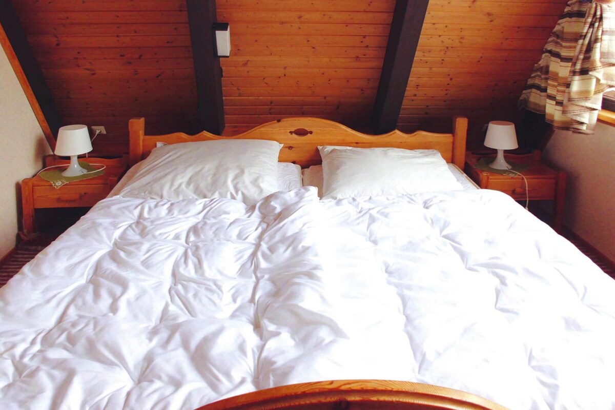 A wooden bed with white bedding in a room with wooden walls and a sloped ceiling.