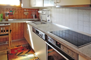 A kitchen with wooden cabinets, a dishwasher, a stove, and a tiled backsplash. - Tennenbronn Holiday Park, Tennenbronn (Schramberg)