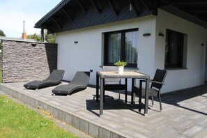 En moderne udendørs terrasse med et bord, stole, en lille potteplante og to liggestole.