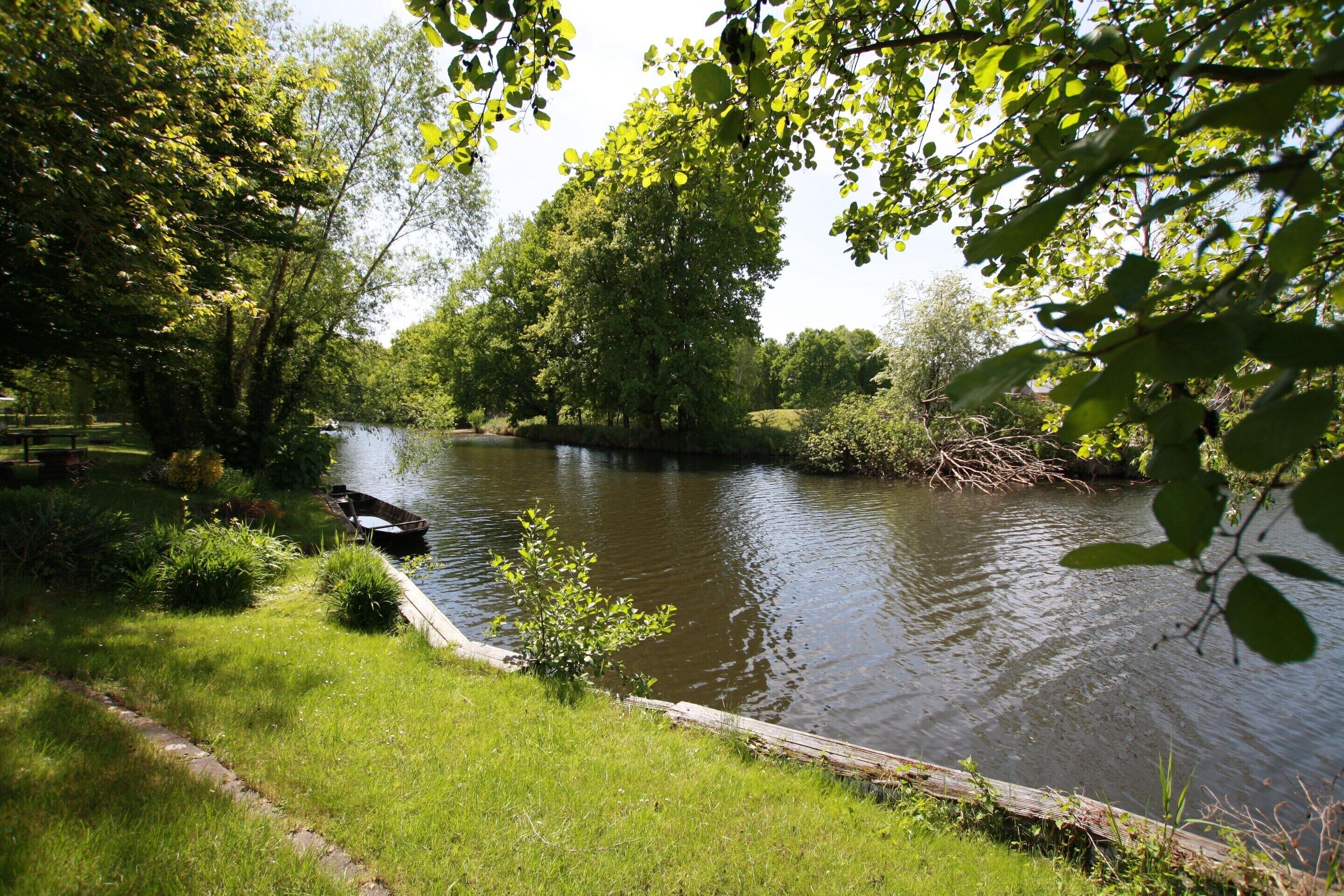 A tranquil riverside setting with a narrow waterway, grassy banks, and dense foliage.