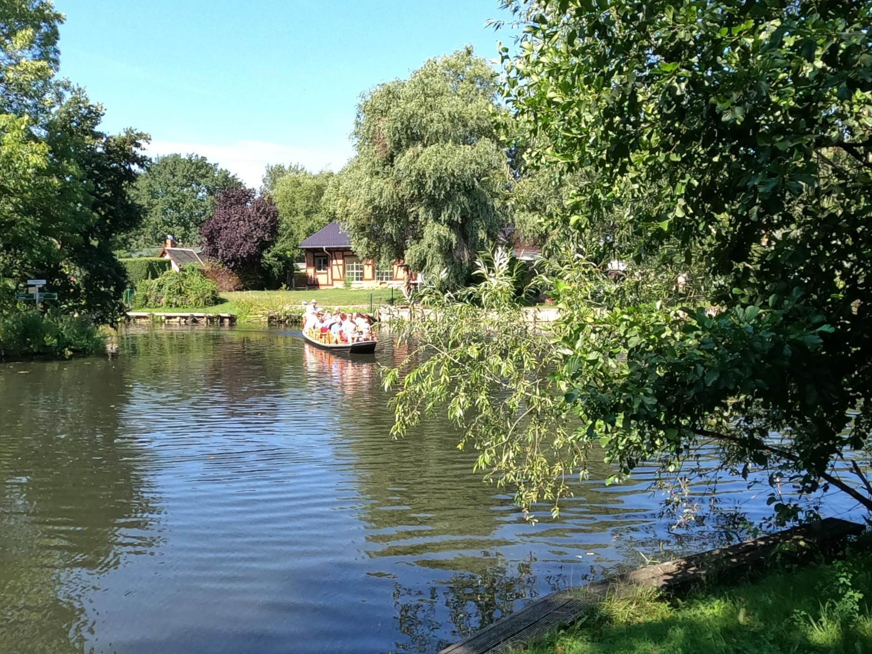Un río tranquilo con una barca llevando pasajeros, rodeado de abundante vegetación y edificios tradicionales.