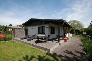Et moderne hus med en patio, der indeholder et bord, stole, grill og en stenvæg.