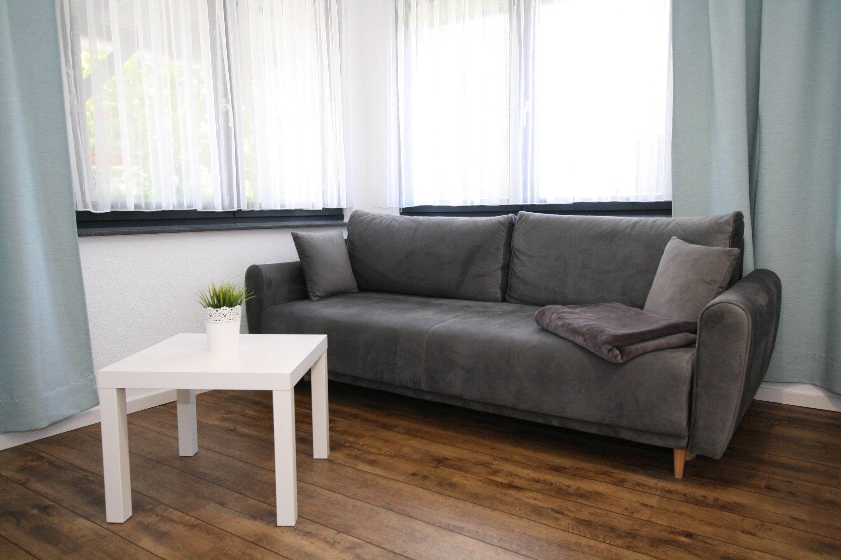A modern living room with a grey sofa, a white table, and a small plant.