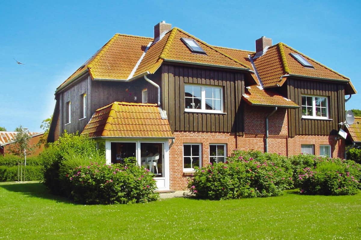 Une maison à deux étages, avec un toit en pente, une cheminée bien visible et un petit porche doté d’une porte vitrée.
