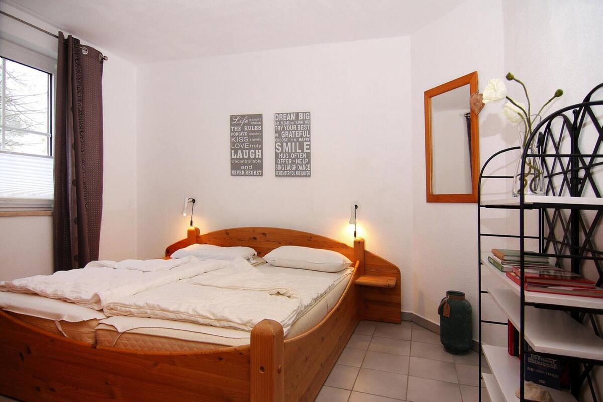 A bedroom with a wooden bed, two bedside lamps, a bookshelf, a mirror, and two motivational posters on the wall.