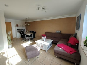 Ein Wohnzimmer mit braunem Sofa, einem weißen Couchtisch und einem Essbereich mit Tisch und Stühlen.