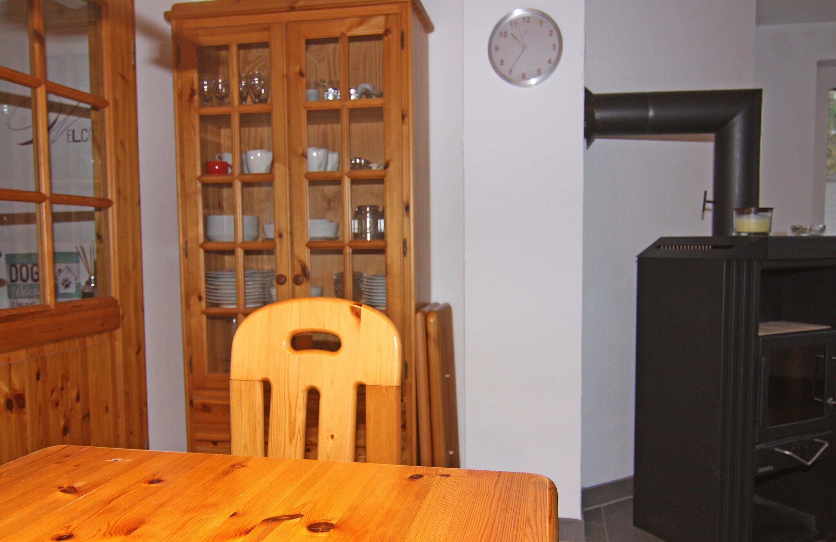 Une table de salle à manger en bois avec des chaises, un buffet en verre contenant de la vaisselle et un poêle noir.