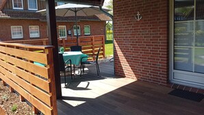 A covered patio with a table and chairs, a wooden bench, and a brick wall with a window. - Holiday Complex Wenkendorf, Fehmarn-wenkendorf (Fehmarn)