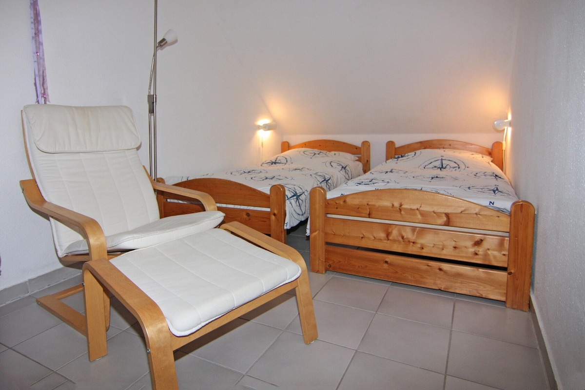 Une petite pièce avec deux lits en bois, une chaise en bois et un lampadaire.