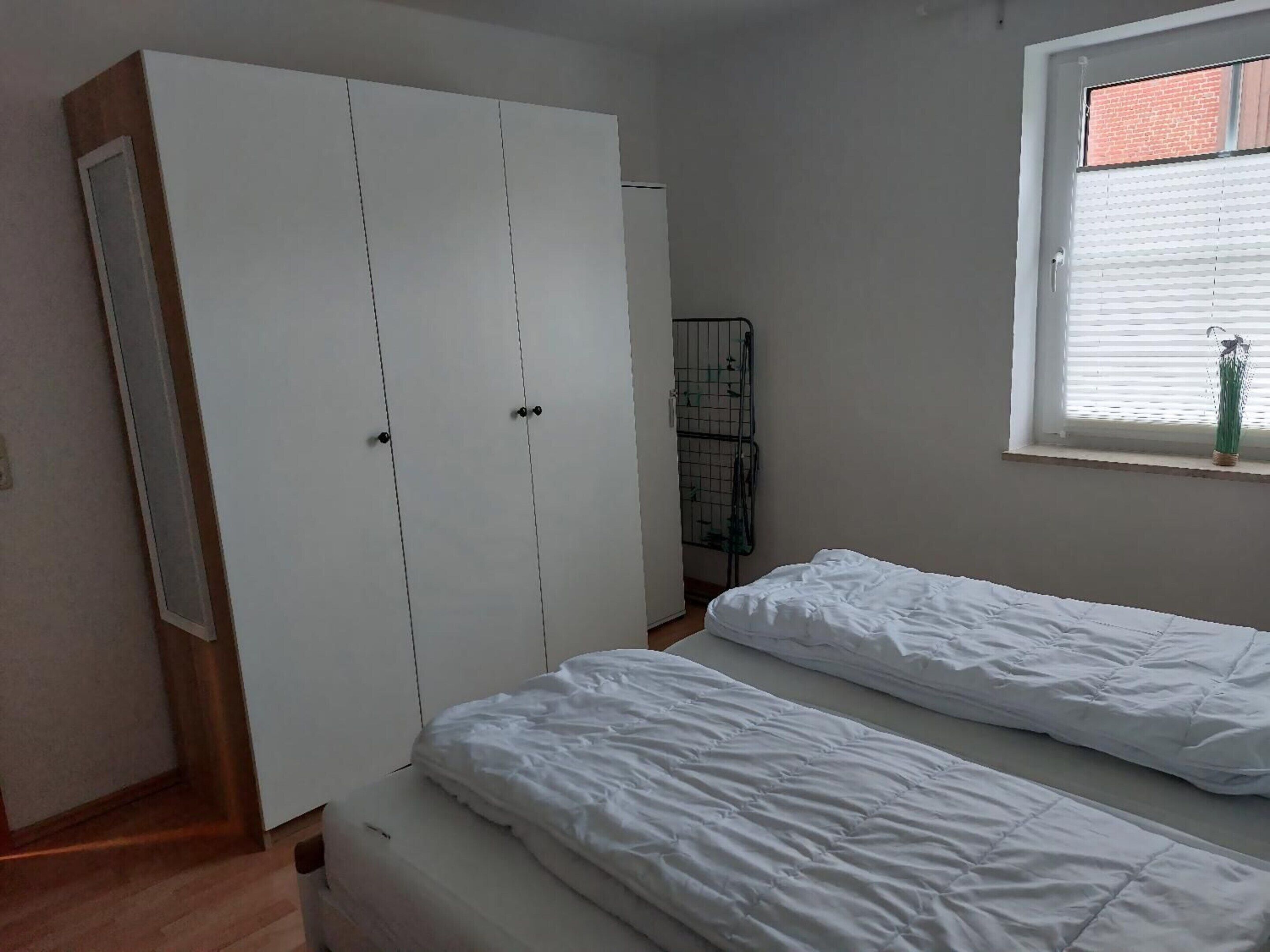 A bedroom with two single beds, a wardrobe, a window with blinds, and a radiator.