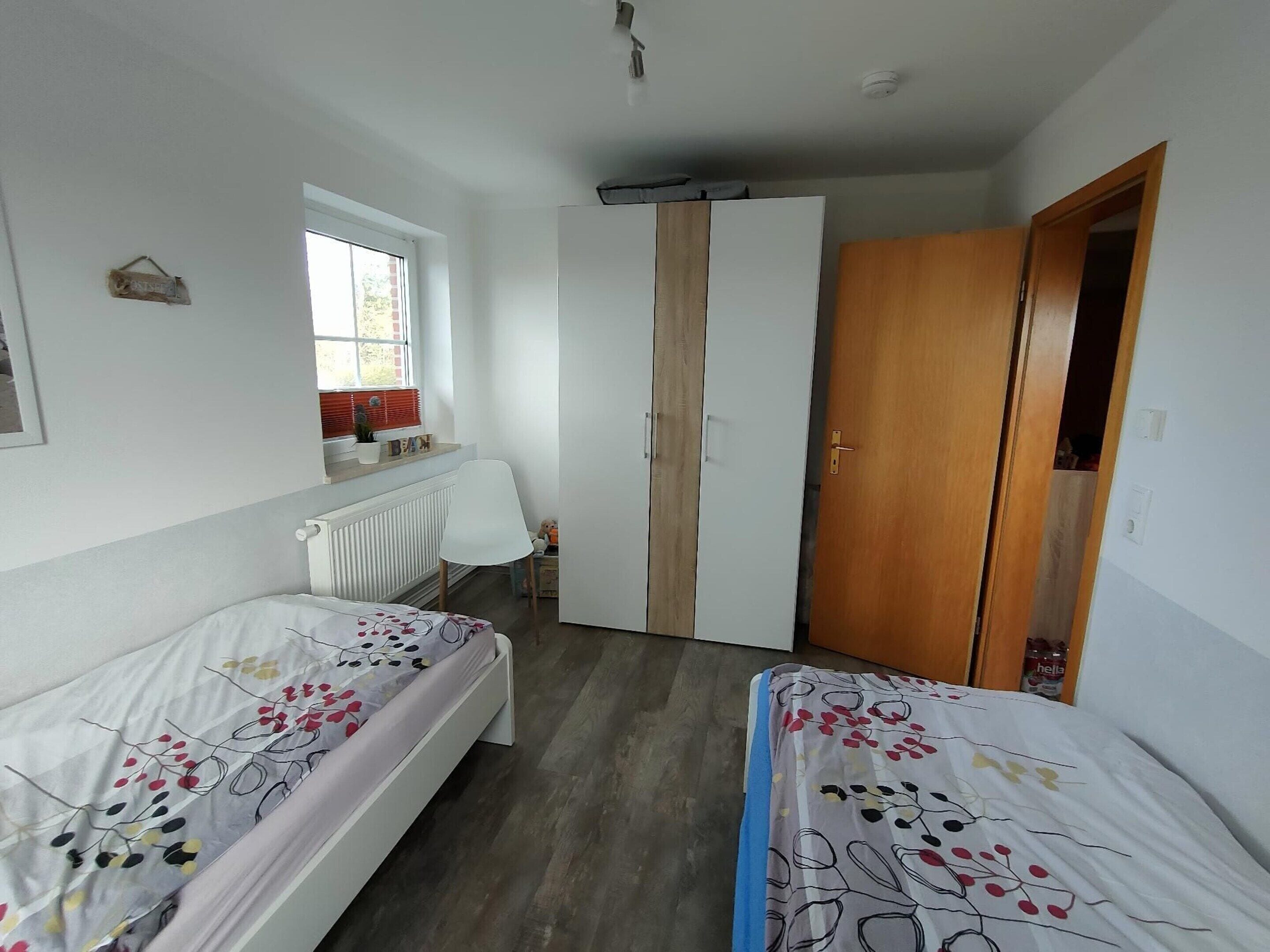 Un dormitorio con dos camas individuales, un radiador, una ventana y un armario.