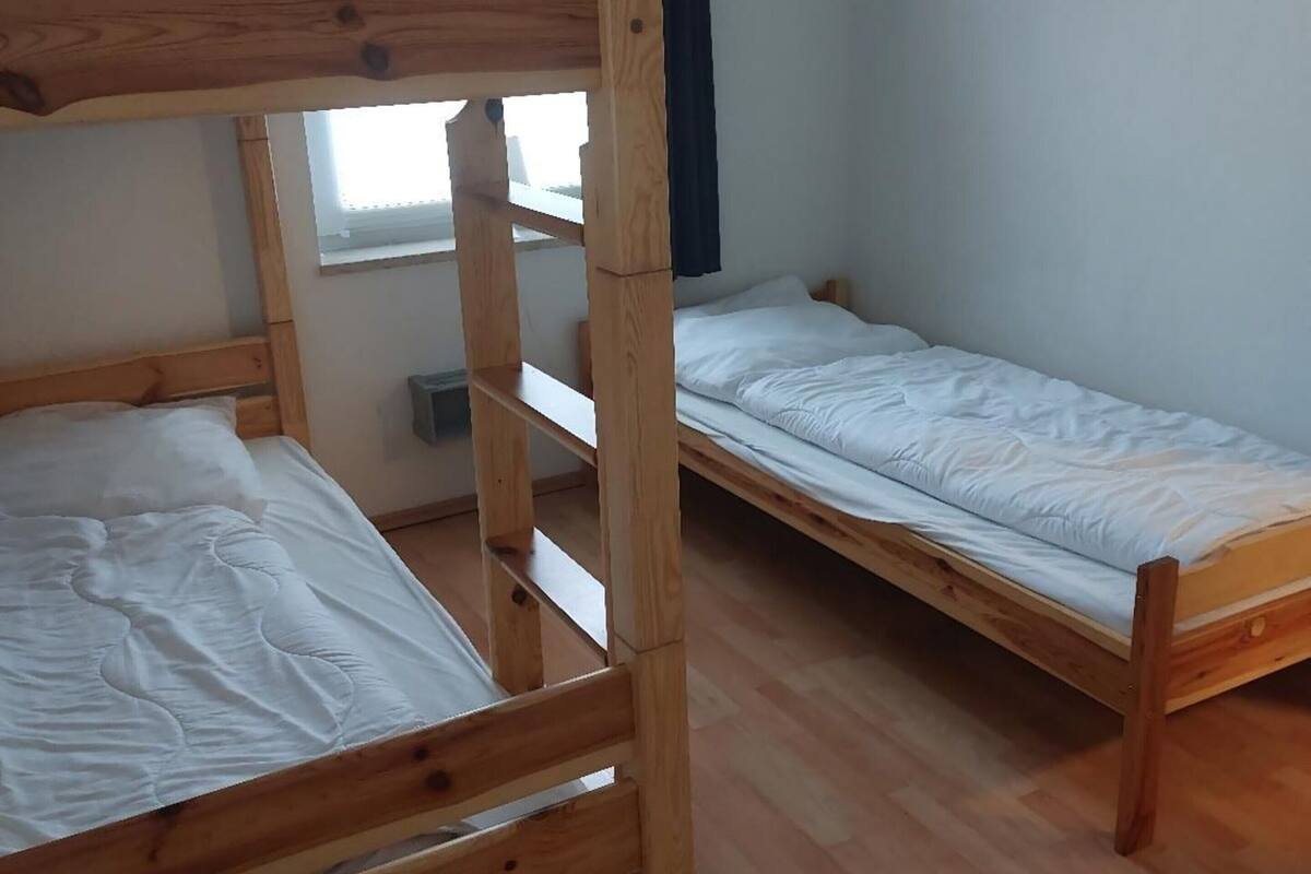 A room with two wooden bunk beds, a window, and a plain white wall.