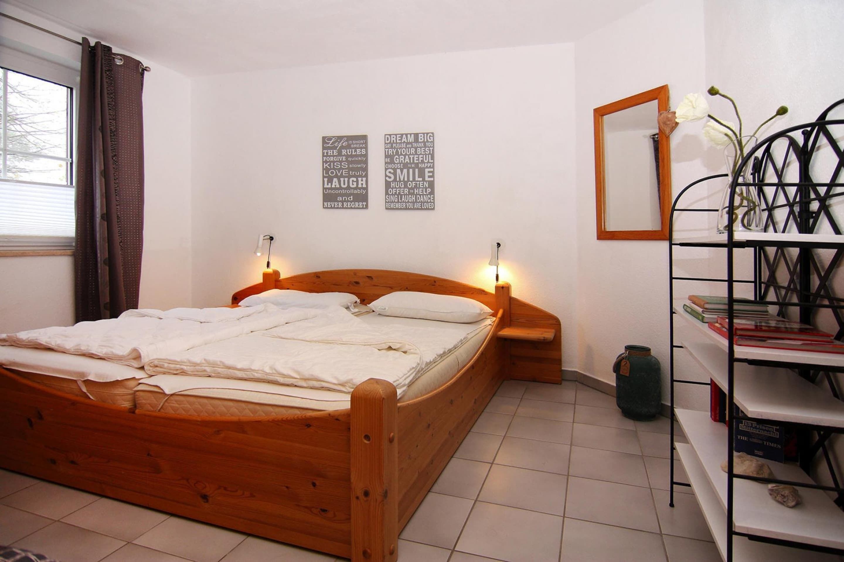 Une chambre à coucher avec un lit en bois, une table de chevet, un miroir et une bibliothèque.
