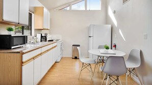 Una cucina moderna con mobili bianchi, un forno a microonde e un lavello. È presente un'area pranzo con un tavolo e sedie bianche.