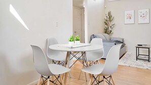 Un soggiorno moderno con un tavolo da pranzo rotondo, quattro sedie bianche, un divano grigio, un piccolo tavolino e due quadri floreali incorniciati appesi al muro.