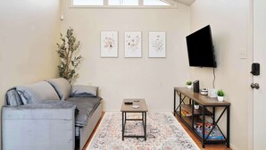 Un soggiorno con un divano grigio, un tavolino, una TV su un mobile e tre quadri floreali incorniciati a parete.