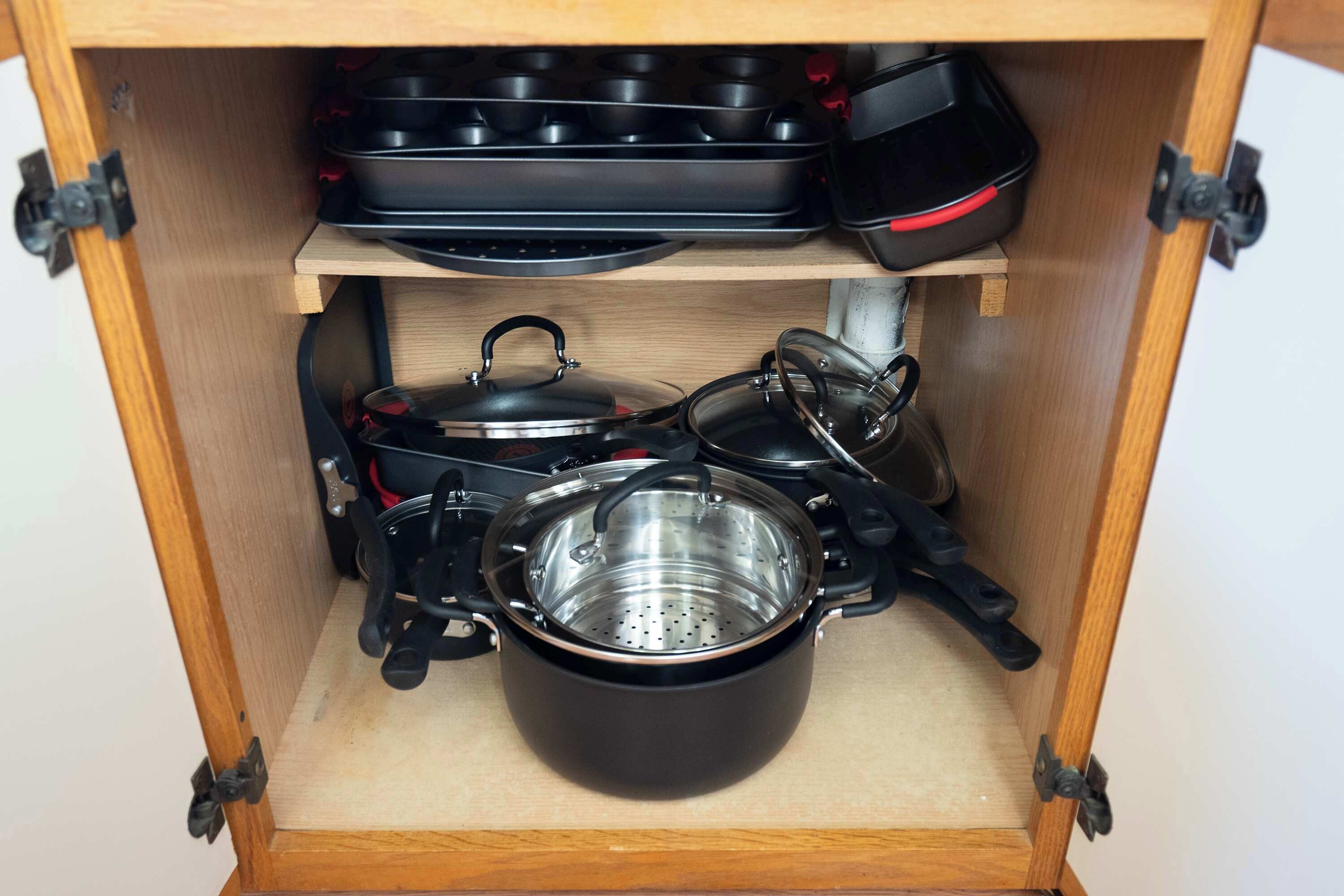 A wooden cabinet with a stovetop, a pot, a kettle, and a pan.