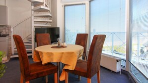 Een eethoek met een ronde tafel, vier stoelen, een televisie en een trap.