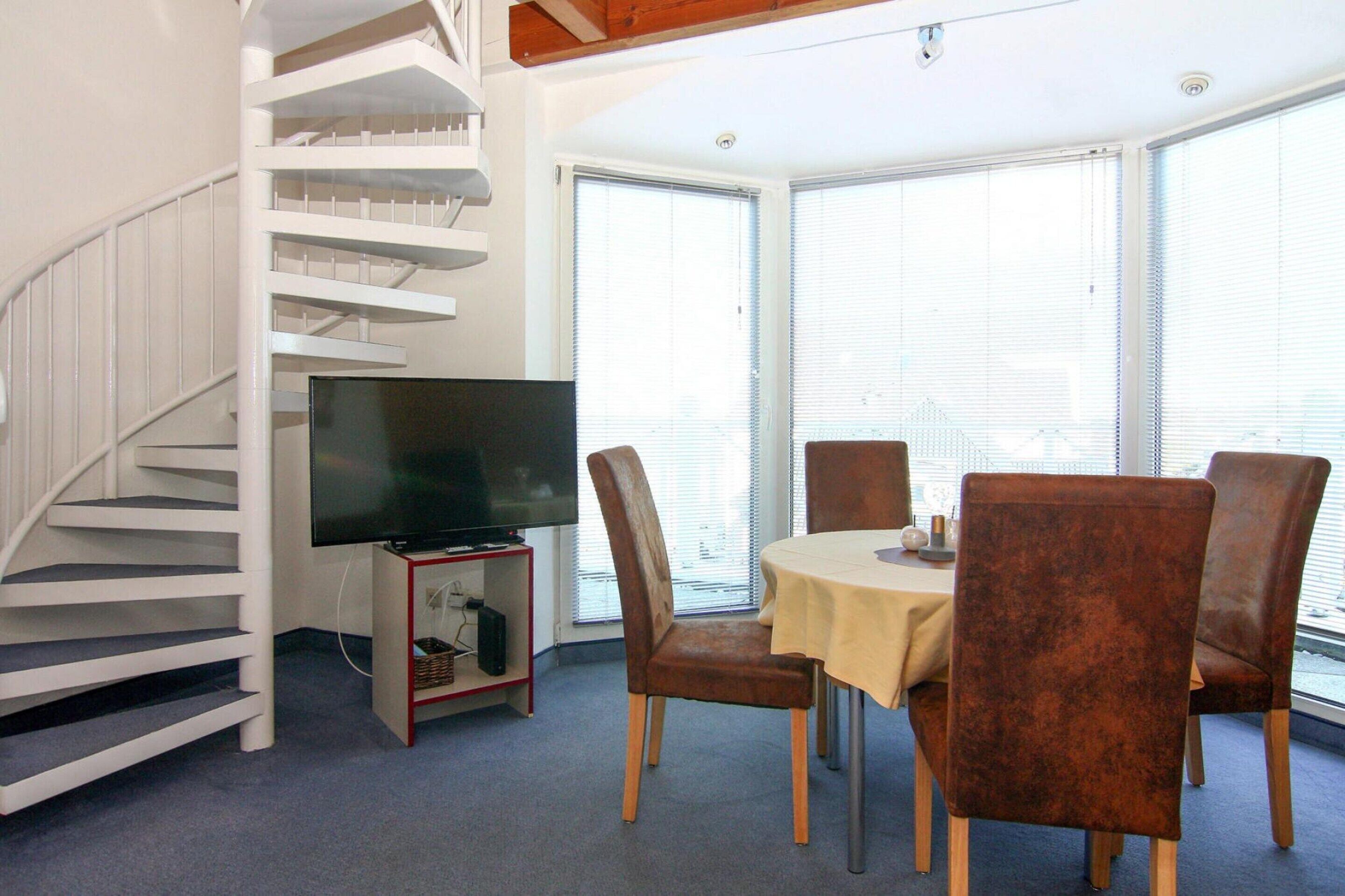 Un coin repas avec une table et des chaises, un téléviseur posé sur un meuble et un escalier.