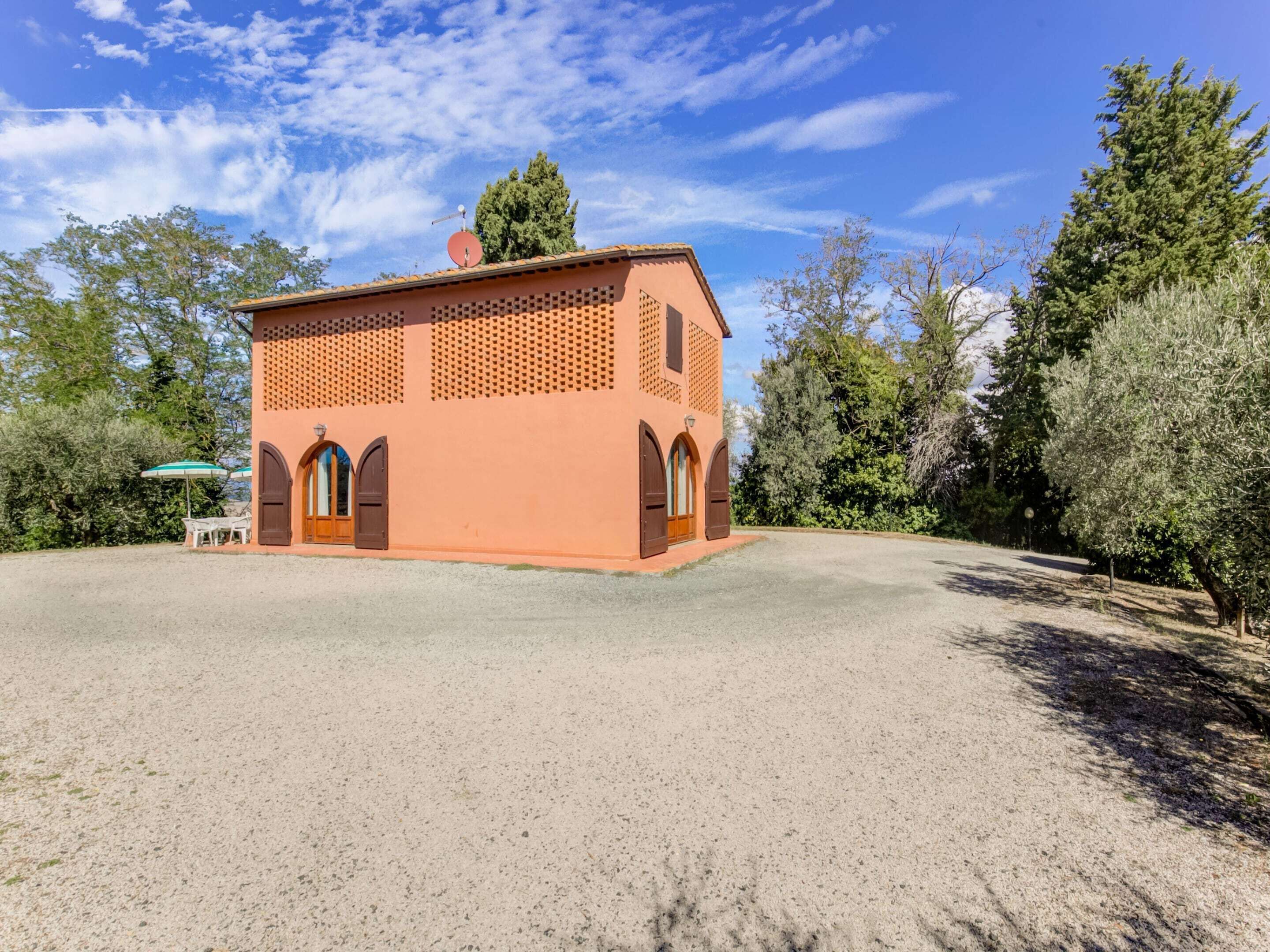 A small, single-story building with a tiled roof, a gravel driveway, and a few trees in the background.