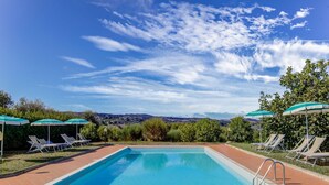 A rectangular swimming pool with clear blue water, surrounded by a tiled deck. There are lounge chairs and umbrellas along the poolside. - Belvilla by OYO Casanova Dependance (Gambassi Terme)