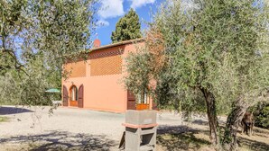 A building with a brick facade, arched windows, and a small courtyard with a stone planter. - Belvilla by OYO Casanova Dependance (Gambassi Terme)