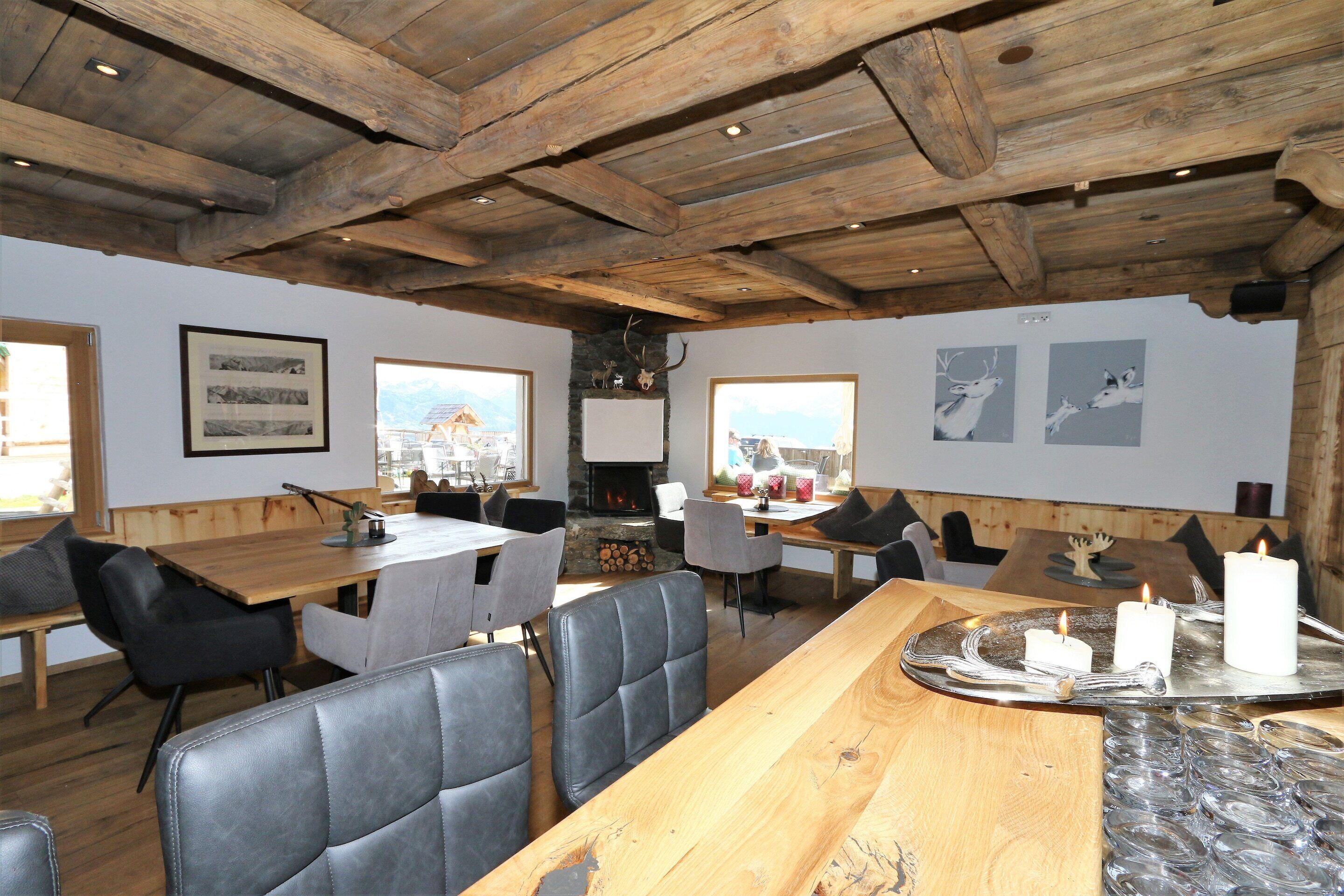 A rustic dining area with wooden tables and chairs, a stone fireplace, and framed pictures on the walls.
