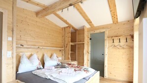 A wooden cabin bedroom with a bed, pillows, a wardrobe, and a door. - Unique Large Alpine Pasture in the Middle of the Zillertal Mountains (Zellberg)