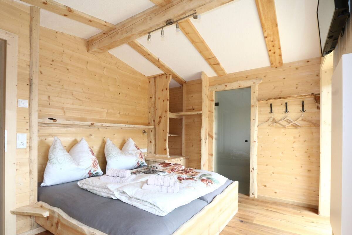 A wooden cabin bedroom with a bed, pillows, a wardrobe, and a door.