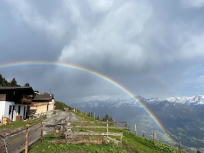 A mountain road with a rainbow, houses, and snow-capped peaks in the background.