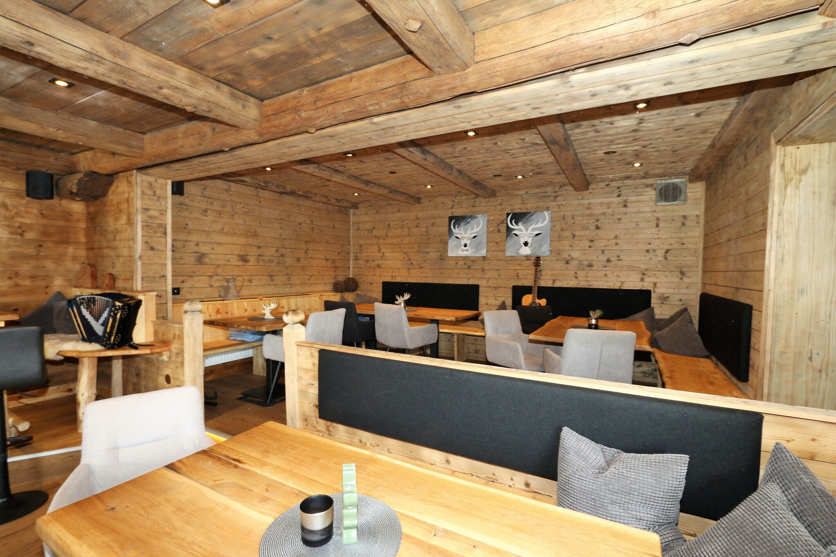 A wooden interior with high ceilings, wooden beams, and a dining area with tables and chairs.