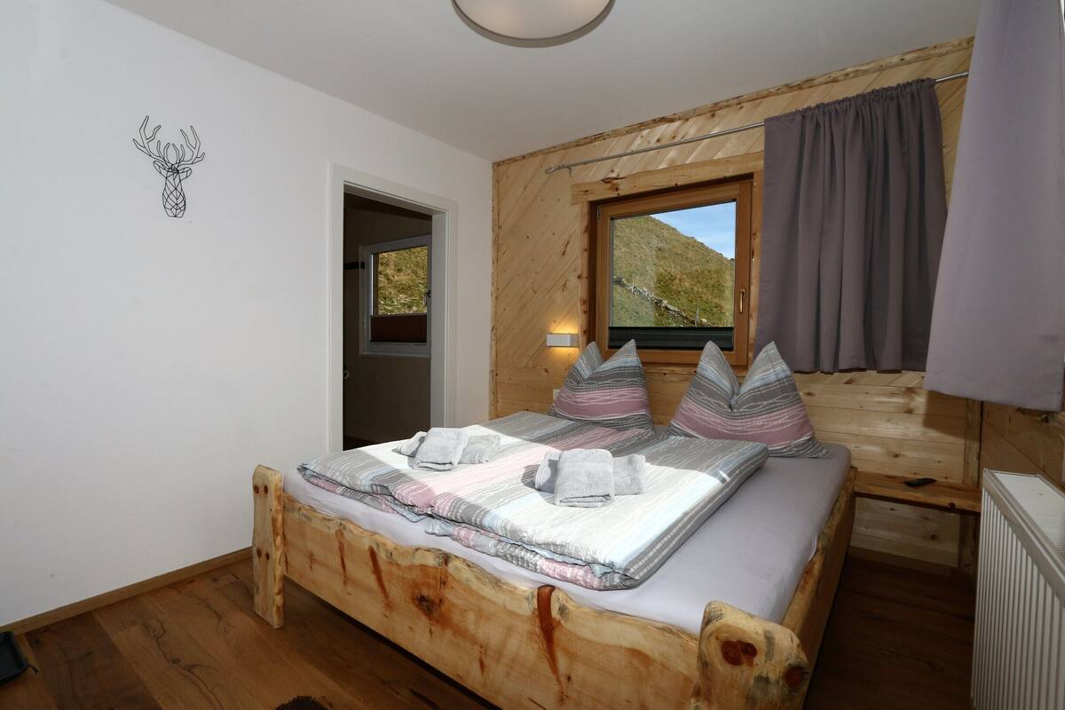 A wooden bed with a view of a mountain, a window with curtains, and a wall-mounted light.