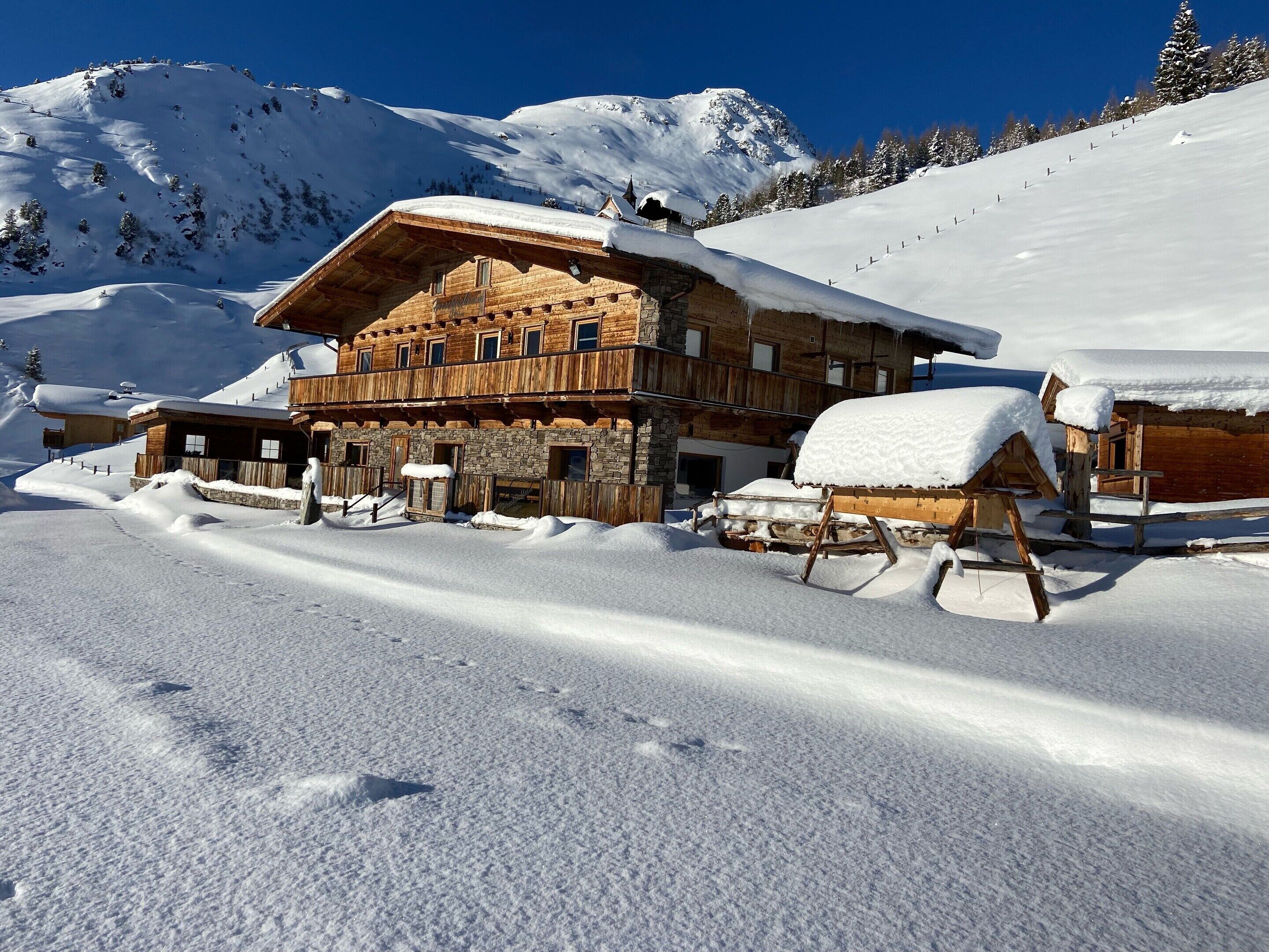 A wooden chalet with a stone foundation, surrounded by snow-covered mountains.