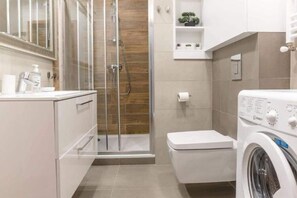 Ein modernes Badezimmer mit einer Duschkabine aus Glas, einer Toilette und einer Waschmaschine mit Frontlader.