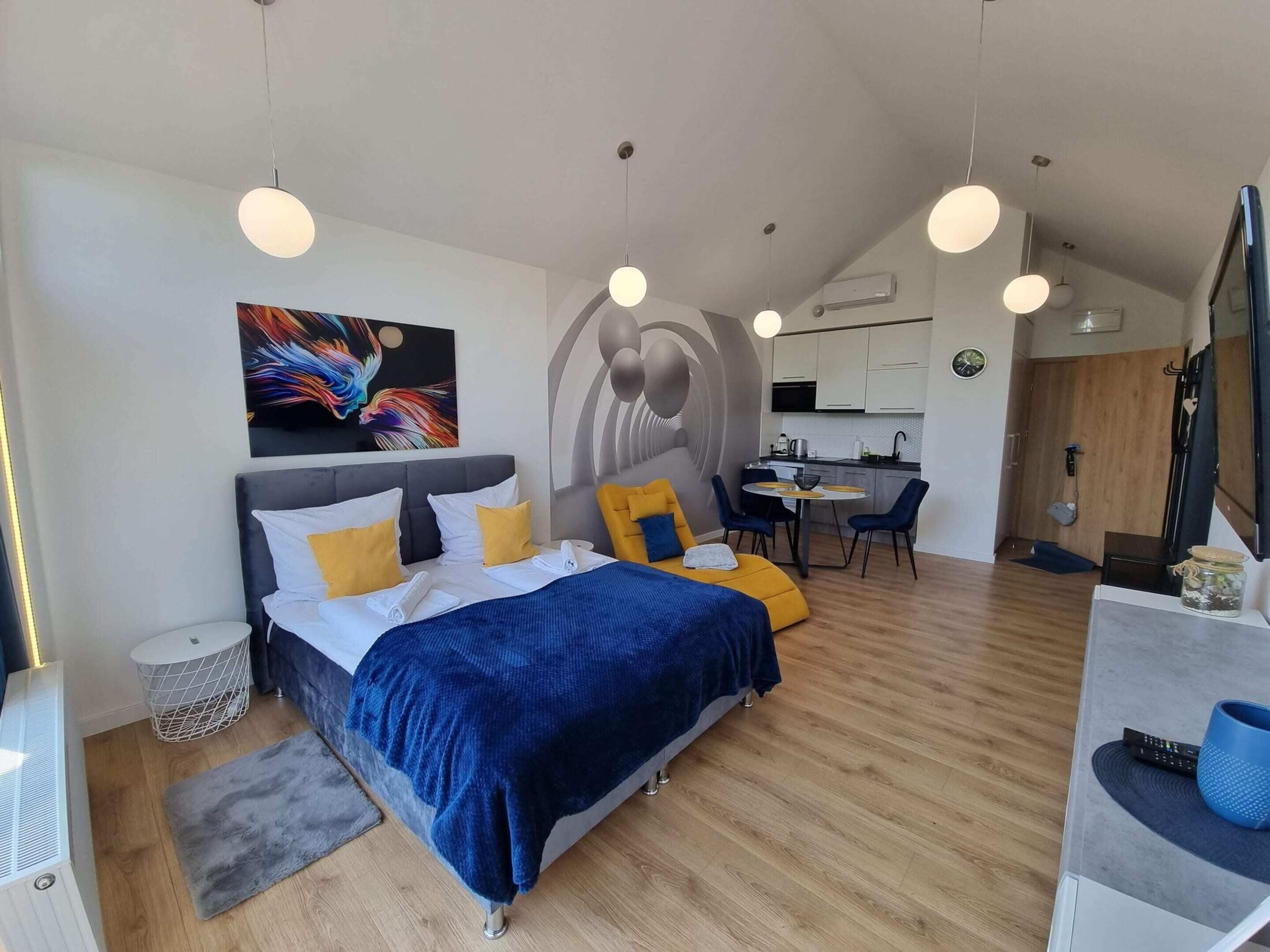 A modern hotel room with a bed, a desk, and a kitchenette.