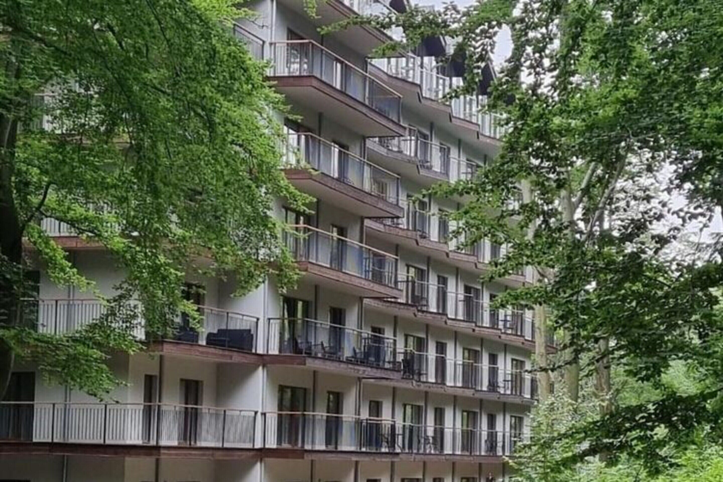 A multi-story residential building with balconies, surrounded by trees.