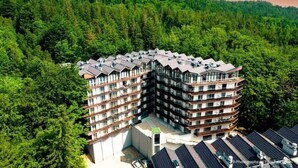 Un hotel de varios pisos con una estructura de esquina peculiar, rodeado de un bosque frondoso.