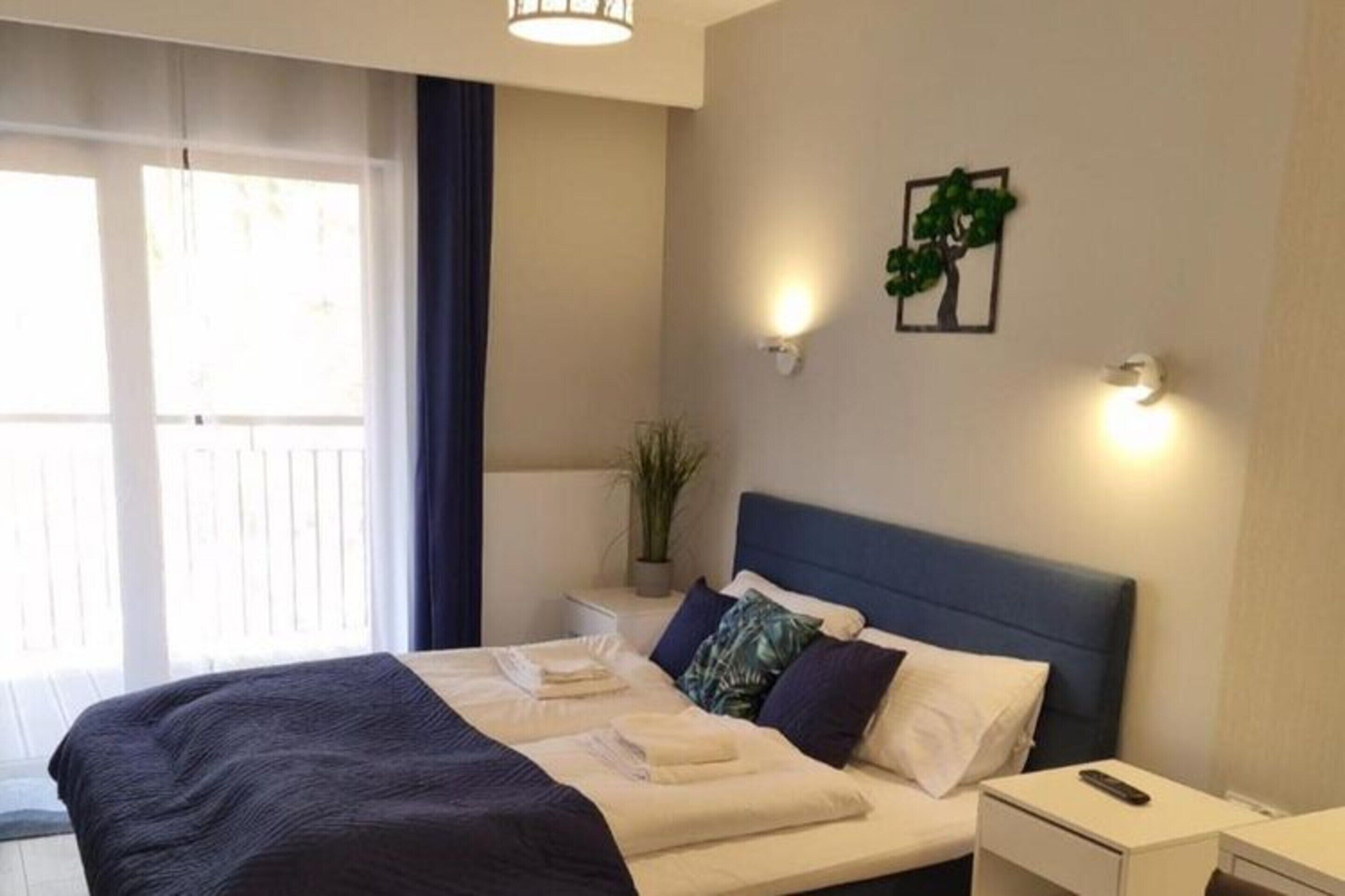 A bedroom with a bed, bedside tables, a wall-mounted light, and a window with curtains.