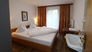 A hotel room with a wooden bed, a bedside table with a lamp, a chair, a sink, and a window with curtains. - Holiday Home Bergheim, Fugen (Fuegen)
