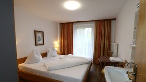 A hotel room with a wooden bed, a bedside table with a lamp, a bathroom with a sink and mirror, and a window with curtains. - Holiday Home Bergheim, Fugen (Fuegen)