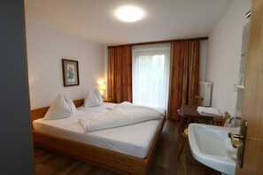 A hotel room with a wooden bed, a bedside table with a lamp, a bathroom with a sink and mirror, and a window with curtains. - Holiday Home Bergheim, Fugen (Fuegen)