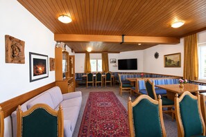 A cozy room with a sofa, a dining table, and a TV. There are wooden beams on the ceiling and a patterned rug on the floor. - Holiday Home Bergheim, Fugen (Fuegen)