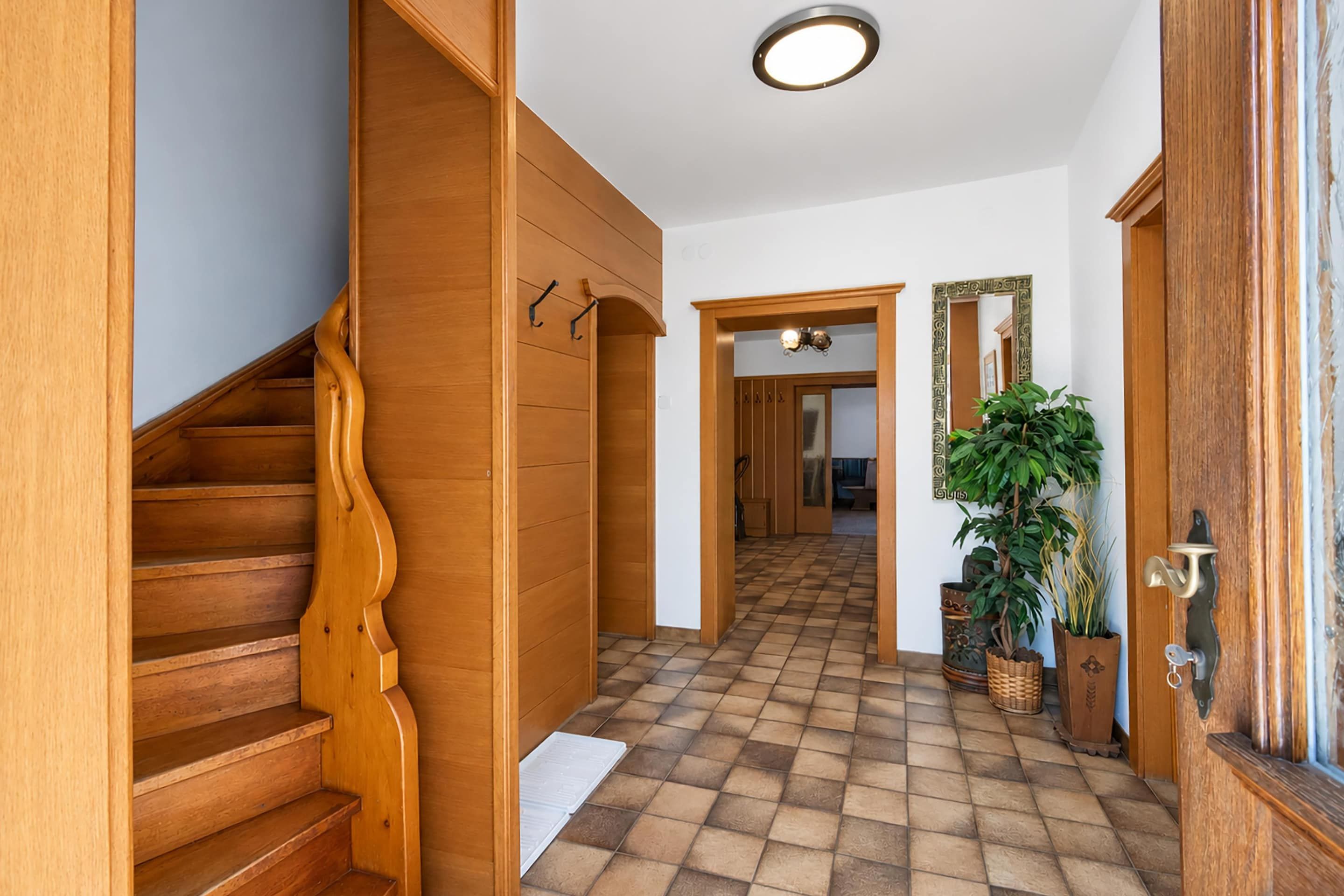 A wooden staircase leading to a hallway with a checkered floor, a mirror, and a door with a decorative handle.