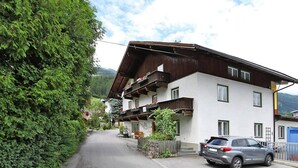 A two-story building with a sloped roof, a balcony with red flowers, and a parked car in front. - Holiday Home Bergheim, Fugen (Fuegen)