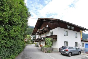 A two-story building with a sloped roof, a balcony with red flowers, and a parked car in front. - Holiday Home Bergheim, Fugen (Fuegen)