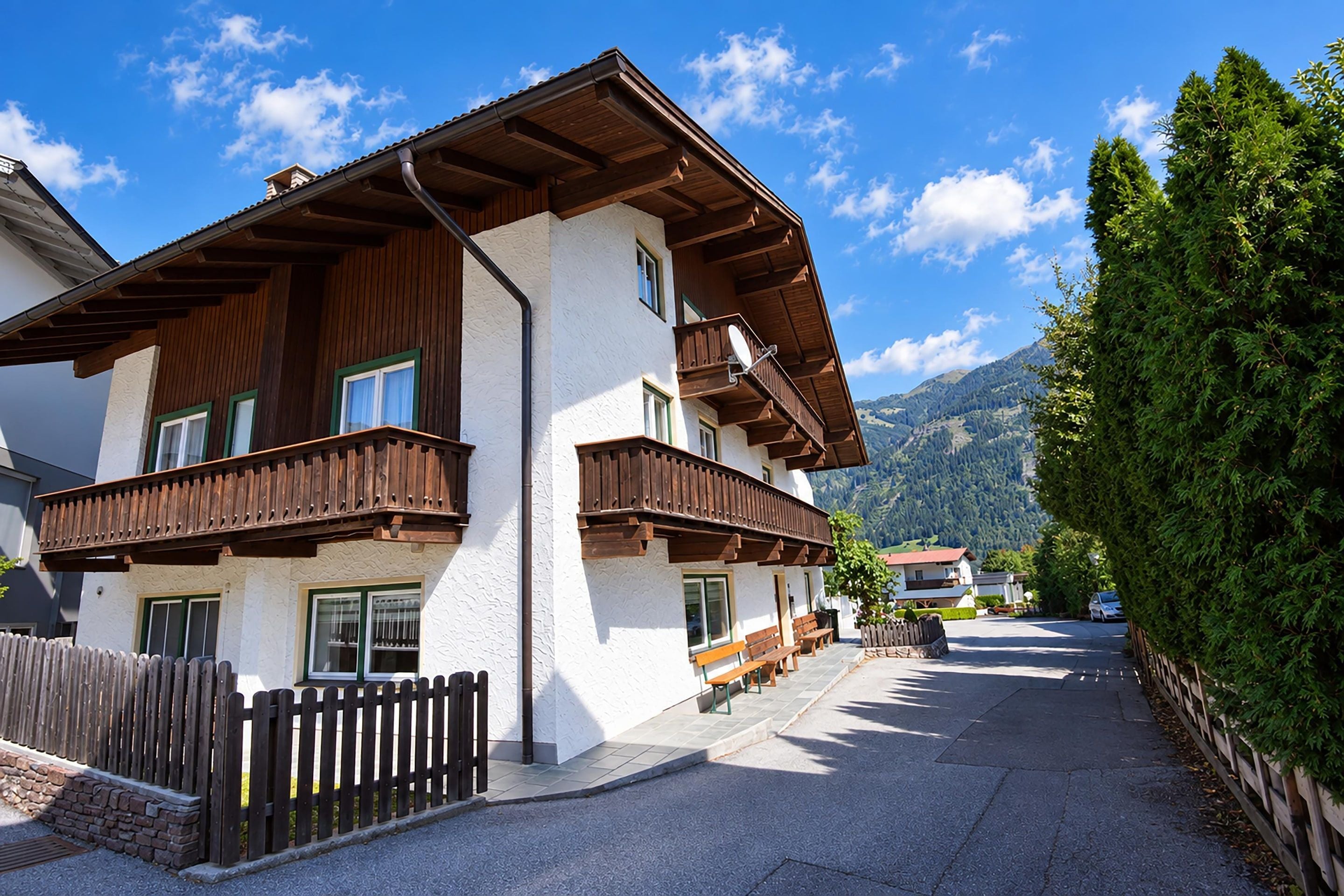 A two-story chalet with wooden balconies, a stone wall, and a view of mountains.