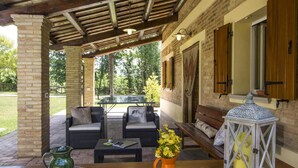 A covered patio area with outdoor furniture, a table with a newspaper, a pitcher, and a vase of flowers. - Belvilla by OYO Villa Vanessa Coccinella (Fano)