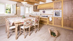 A rustic kitchen with wooden beams, a dining table with chairs, a stove, and cabinets. - Belvilla by OYO Villa Vanessa Coccinella (Fano)