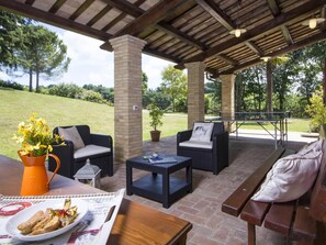 An outdoor patio with wicker furniture, a brick column, and a table with food. - Belvilla by OYO Villa Vanessa Coccinella (Fano)