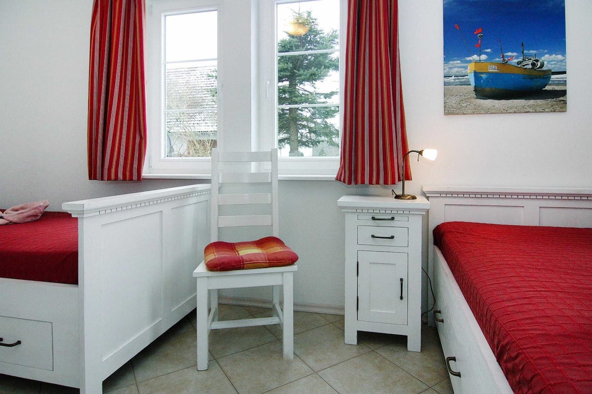 A bedroom with two beds, a chair, a nightstand, and a window with curtains.